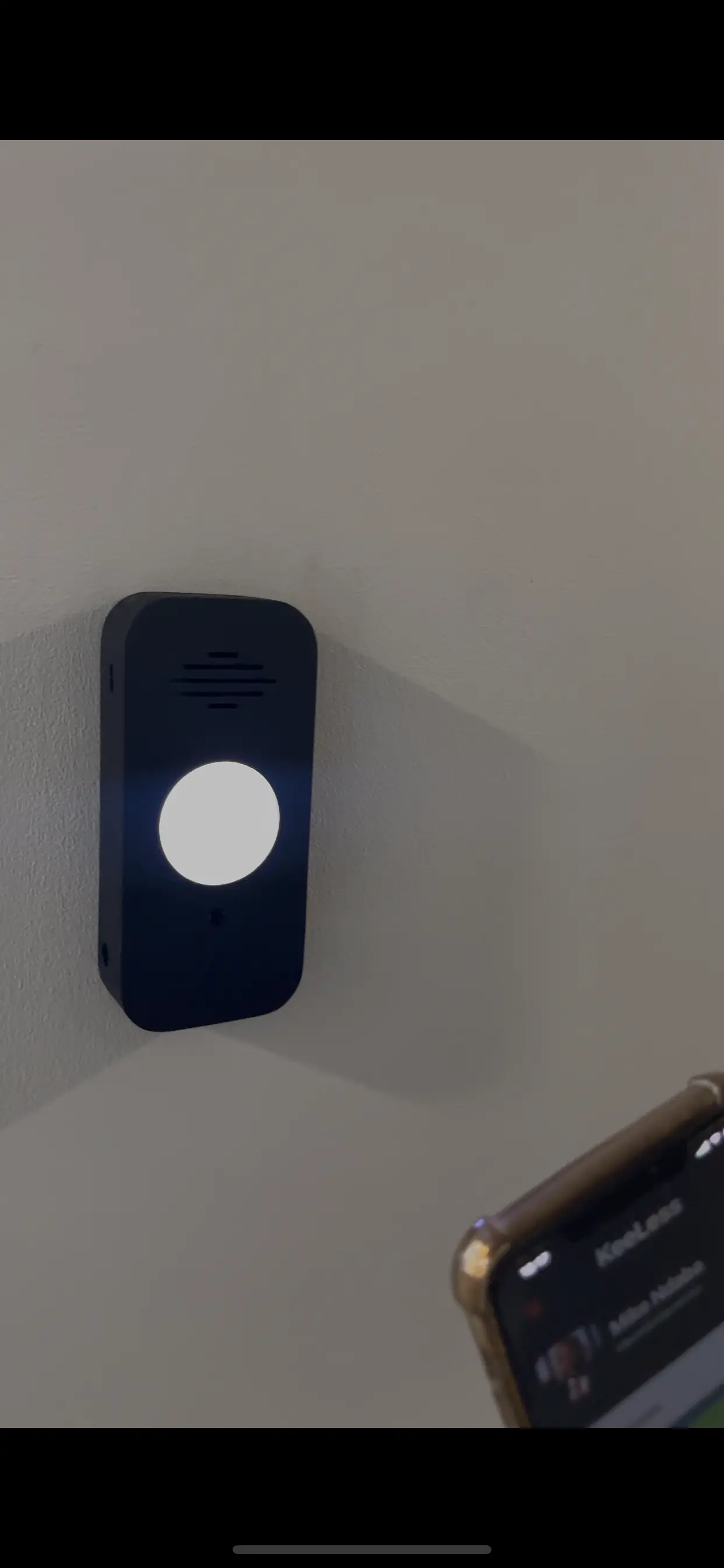 A KeeLess reader unlocking on a wall while a phone running the KeeLess app is held nearby